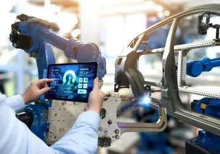 A photo of a person holding a tablet with graphs up to an assembly robot.